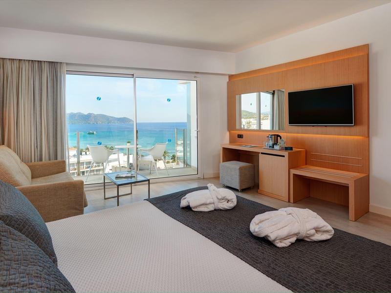 Modern hotel room with double bed, sofa, large window, and sea view.