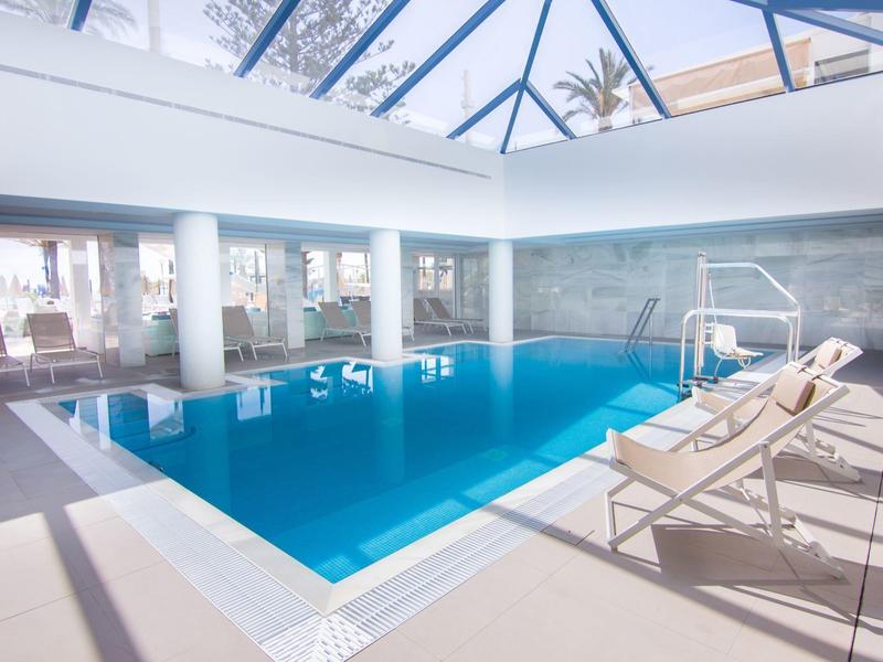 Indoor pool with modern lounge chairs and large glass roof allowing natural light inside.