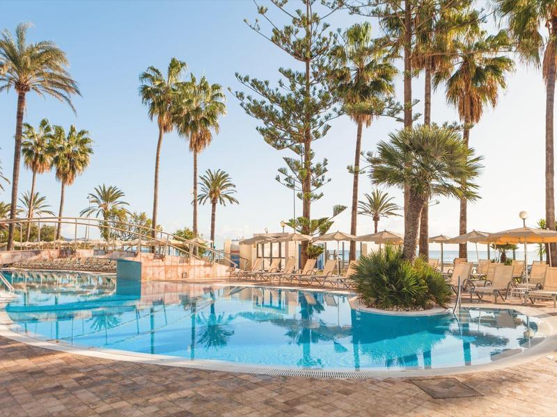 Round pool with sun loungers and palm trees at a sunny vacation spot.