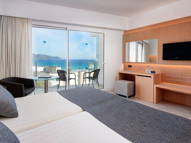 Modern hotel room with balcony and sea view, bright tones, and comfortable furniture.