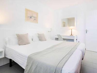 Helles Schlafzimmer mit Doppelbett, grauer Decke, weißen Wänden, Nachttischlampen und Spiegel.