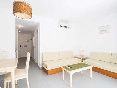 Heller, moderner Wohnraum mit hellen Sofas, weißem Tisch, Esstisch und Holzlampe an der Decke.