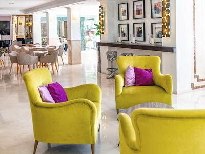 Heller, moderner Wohnraum mit gelben Sesseln, violetten Kissen und mehreren gerahmten Bildern an der Wand.