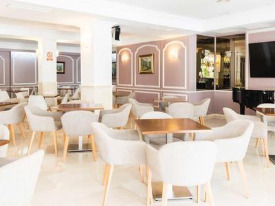 Heller, moderner Speiseraum mit weißen Stühlen, Holztischen und großem Flachbildschirm an der Wand.