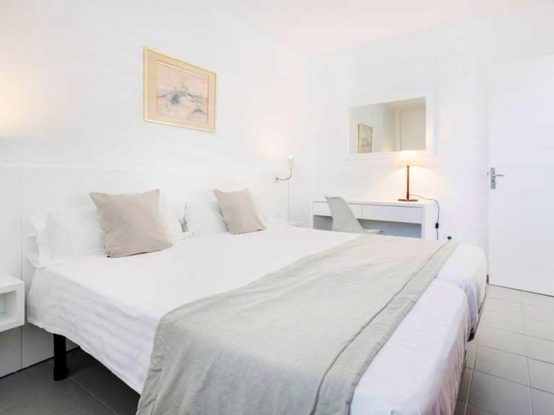 Helles Schlafzimmer mit Doppelbett, grauer Decke, weißen Wänden, Nachttischlampen und Spiegel.