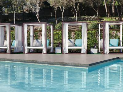 Moderner Pool mit klarem Wasser und weißen Cabanas am Rand, umgeben von Büschen und Bäumen.
