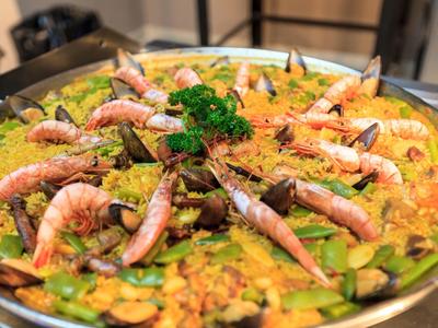 Große Paella mit Garnelen, Erbsen, Karotten und Petersilie, serviert in einer flachen Metallpfanne.
