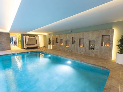 Innenpool mit blauen Wasser, beige Fliesenboden, Wandnischen und Pflanzen in weißen Töpfen.