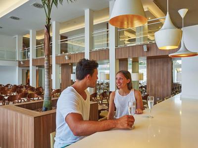 Junges Paar sitzt an heller Bar in modernem, großzügigem Cafe mit Holz- und Glasakzenten.
