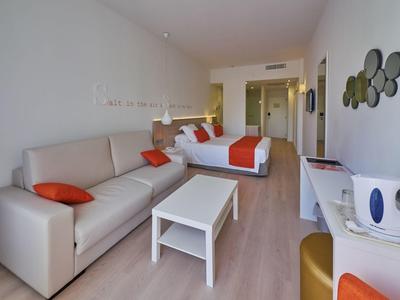 Modern eingerichtetes Hotelzimmer mit Doppelbett, Sofa, Tisch und hellem Holzboden.