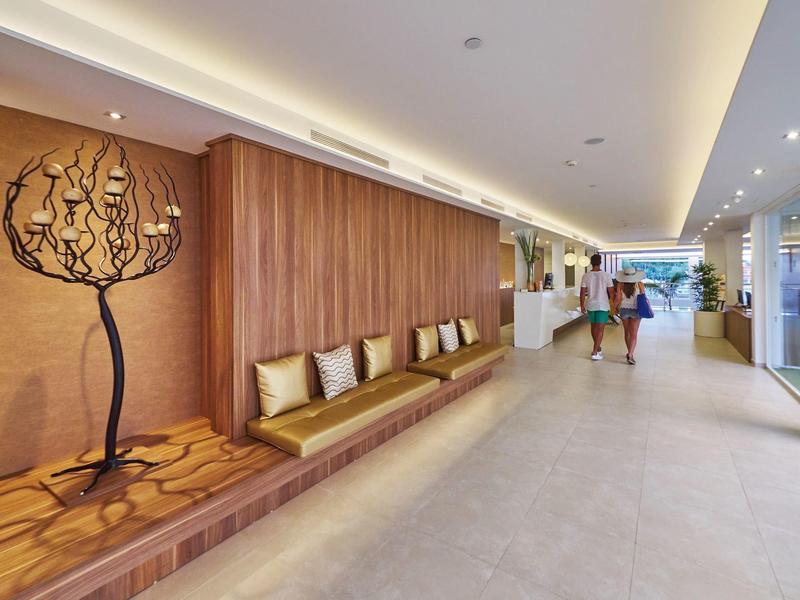 Nowoczesna przestrzeń holu hotelowego z drewnianymi ławkami i ozdobnym drzewem na ścianie.