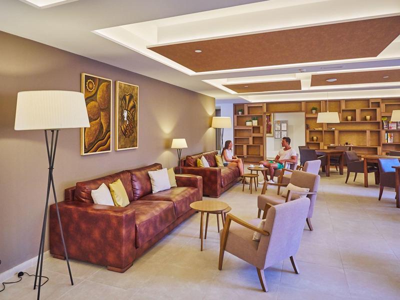 Nowoczesny hotelowy salon z sofą, fotelami, stolikami i regałem na książki w tle.