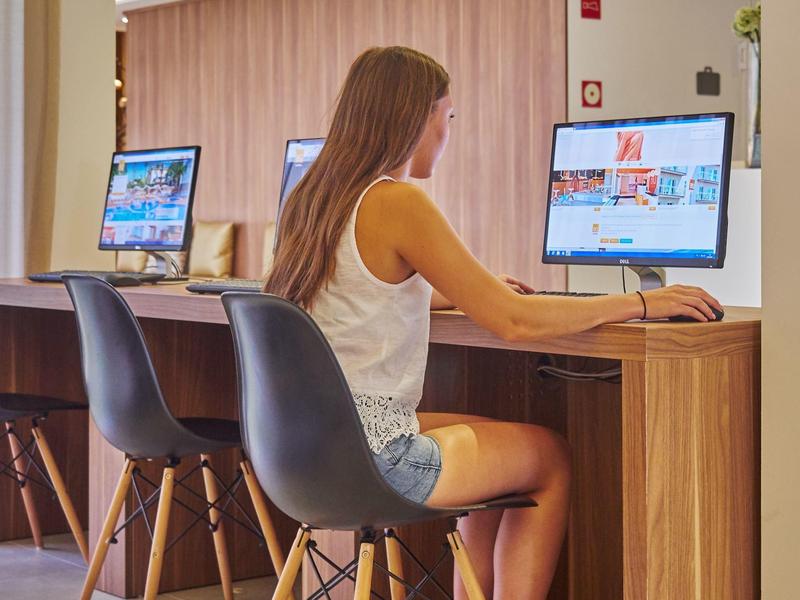 Kobieta siedzi w nowoczesnej przestrzeni roboczej hotelu, korzystając z monitora.