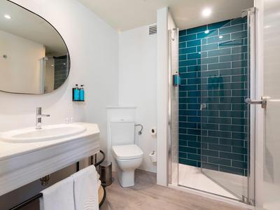 Baño moderno con inodoro blanco, gran espejo ovalado y ducha con azulejos azules.