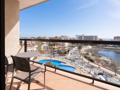 Balcón con silla y mesa con vistas a la marina, botes y una zona de piscina bajo un clima soleado.