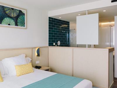 Habitación de hotel moderna con cama doble, pared de ducha turquesa y cuadro decorativo.