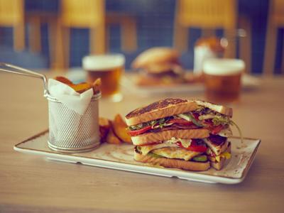 Sándwich con carne y verduras, acompañado de papas fritas y cerveza sobre una mesa de madera.