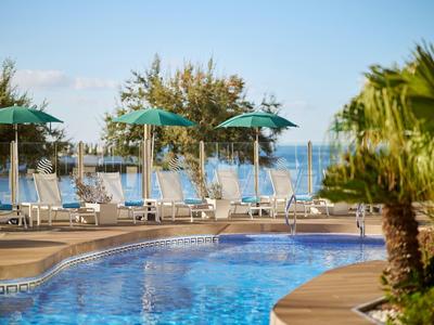 Área de piscina vacía con tumbonas, sombrillas y palmeras bajo cielo despejado