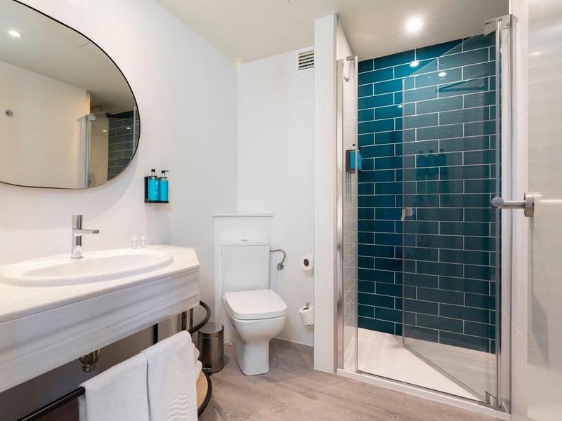 Baño moderno con inodoro blanco, gran espejo ovalado y ducha con azulejos azules.