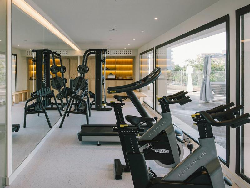 Sala de fitness moderna con equipos de entrenamiento y paredes de vidrio con vista al exterior.