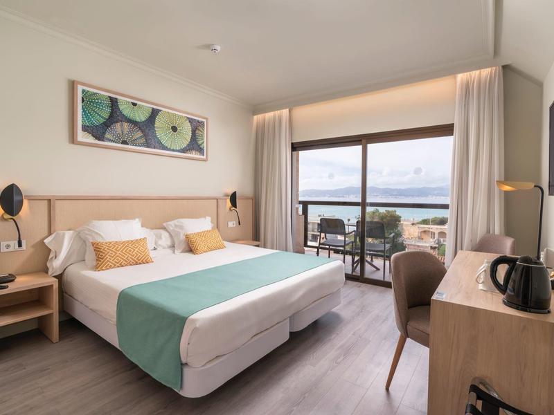 Habitación de hotel luminosa con cama doble, escritorio, balcón con vista al mar y decoración moderna.
