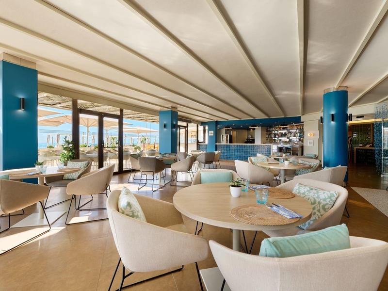 Moderna zona de salón de hotel con sillas cómodas y grandes ventanas con vista al mar.