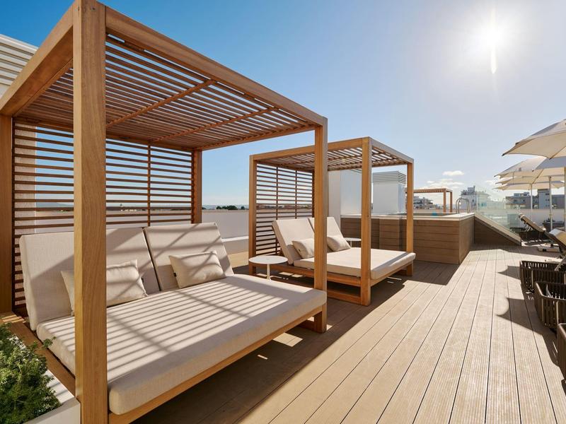 Terraza en la azotea soleada con tumbonas de madera y sombrillas, cielo despejado al fondo.