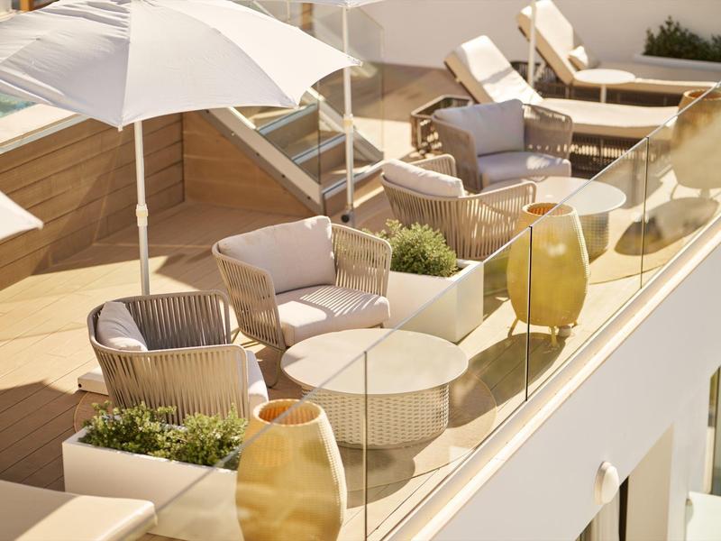 Balcón moderno de hotel con asientos, plantas y sombrillas.