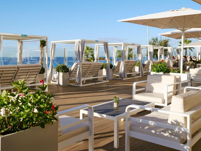 Zona exterior moderna con muebles blancos y camas de día en una terraza de madera con vistas al mar.