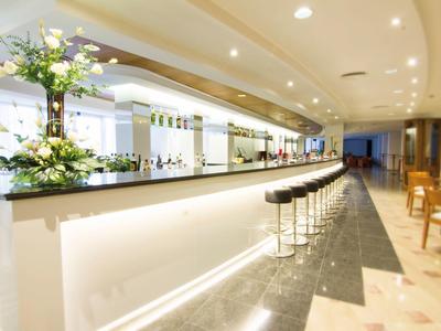 Moderne hotelbar met hoge krukken, verlichte toonbank en bloemendecoratie.