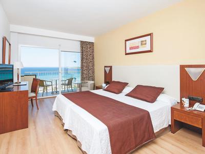 Gezellige hotelkamer met tweepersoonsbed, balkon met uitzicht op zee, houten meubels en lichte muren.