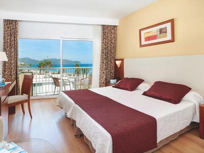 Hell eingerichtetes Doppelzimmer mit Balkon, Meerblick, Fernseher und Holzboden.