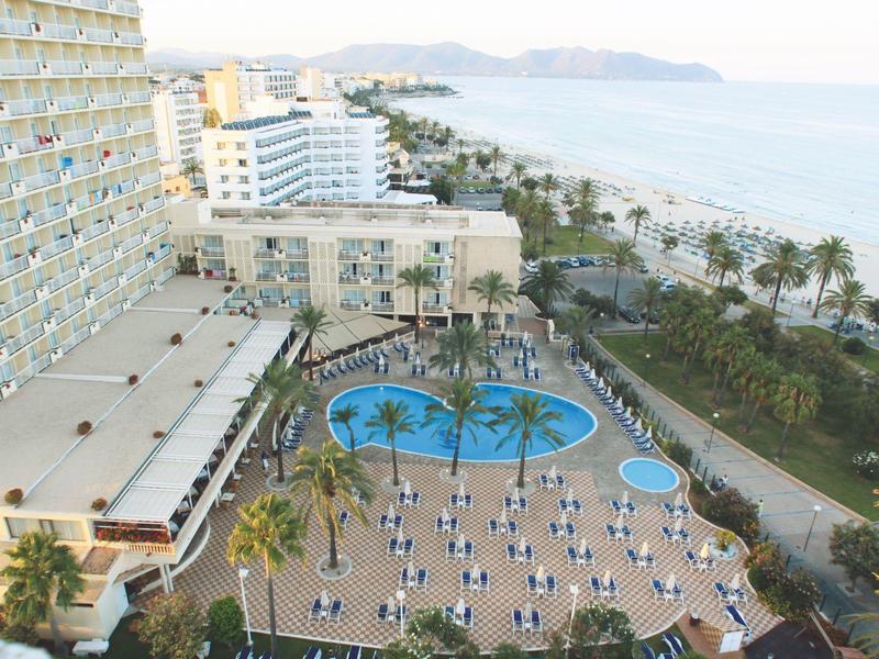 Luchtfoto van hotelzwembad met palmbomen, ligstoelen en zeezicht.