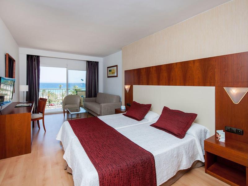 Hotelkamer met tweepersoonsbed, rode accenten, bureau, bank en zeezicht via raam