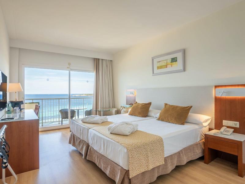 Hotelkamer met twee bedden, balkon met uitzicht op zee en moderne inrichting.