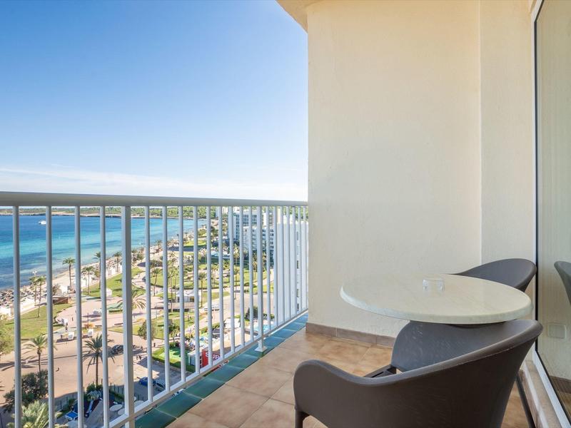 Balkon met tafel en stoelen met uitzicht op strand en oceaan onder een heldere hemel.