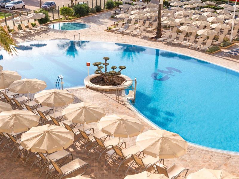 Gebogen buitenzwembad met veel beige ligbedden en parasols.