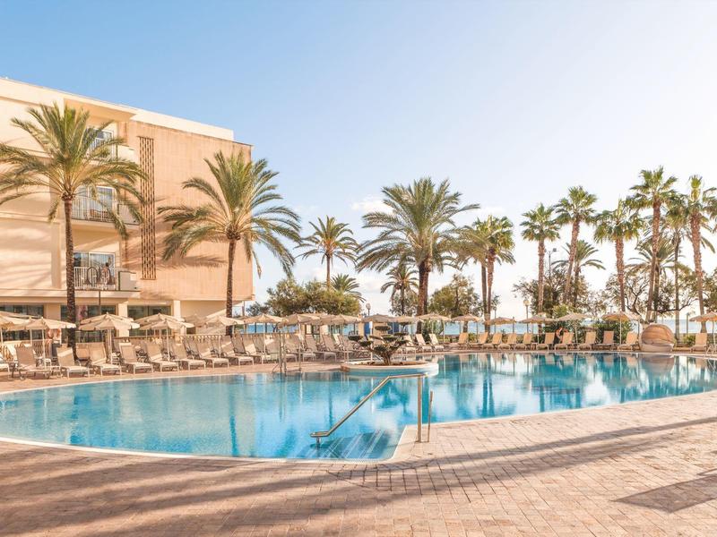 Zonnig buitenzwembad omringd door ligstoelen en palmbomen bij een hotelresort.