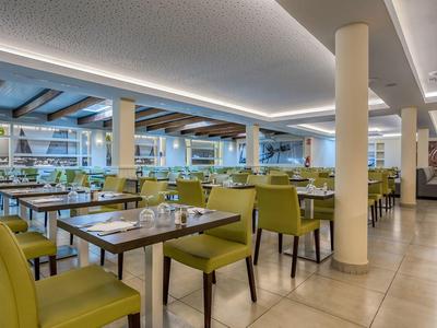 Modernes Restaurant mit grün gepolsterten Stühlen, hellen Wänden und großem Fensterfrontbereich.