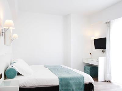 Helles, minimalistisches Schlafzimmer mit Doppelbett, grüner Tagesdecke, Wandlampen und Fernseher.