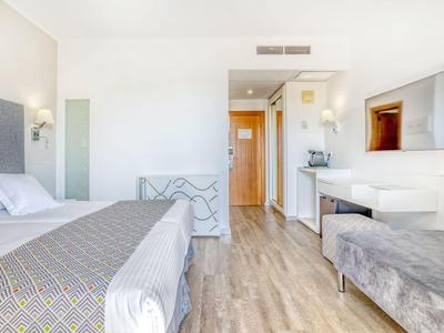 Camera d'hotel moderna con letto matrimoniale, TV a schermo piatto e panca in toni neutri.