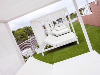 Weiße Daybeds mit Dach auf grünem Kunstrasen in einer Reihenanordnung unter offenem Himmel.