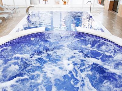 Innenbereich mit sprudelndem Whirlpool im Vordergrund und Schwimmbecken im Hintergrund.