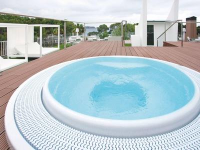Moderner Whirlpool mit klarem Wasser auf großer Holzterrasse unter bewölktem Himmel.