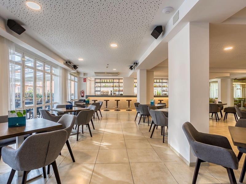 Helles Café mit modernen grauen Stühlen, Holztischen und großer Fensterfront im Tageslicht.