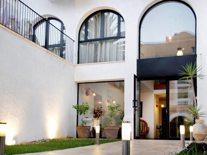 Hotel mit großen, bogenförmigen Fenstern und Eingang, umgeben von Pflanzen und moderner Beleuchtung.