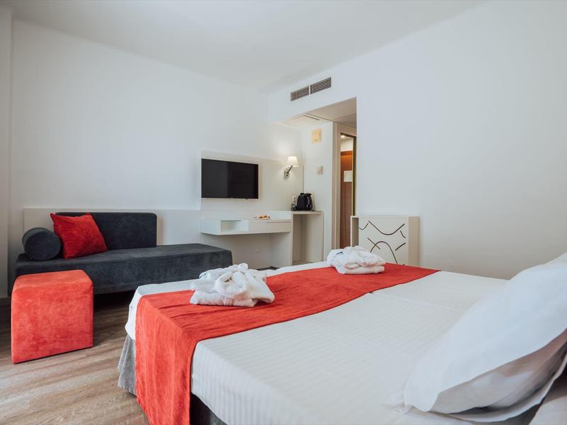 Modernes Hotelzimmer mit einem Bett, Sofa, Fernseher und rotem Akzent in Dekoration und Möbeln.