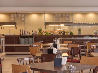 Moderner Speisesaal mit Holztischen und Stühlen, Buffetraum im Hintergrund.