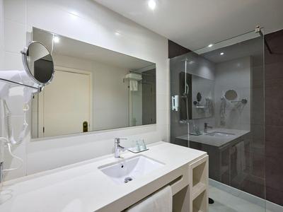 Modernes Hotelbad mit großer Glasdusche, weißem Waschbecken und großem Spiegel.