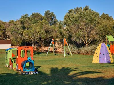 Bunter Kinderspielplatz mit Lokomotive, Klettergeräten und Schaukeln auf grünem Rasen unter blauem Himmel.